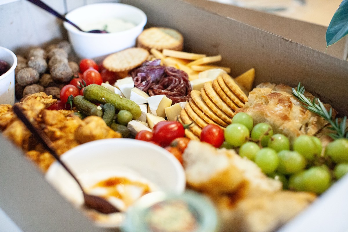 An open Daai Platter Boks catering box with chicken skewers, frikkadelle, focaccia, cheese and grapes